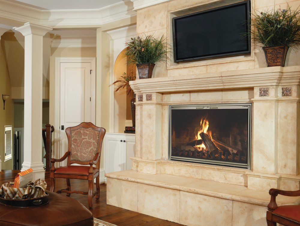 Fireplace with lit fire, TV above, flanked by potted plants, in a tan-colored room.