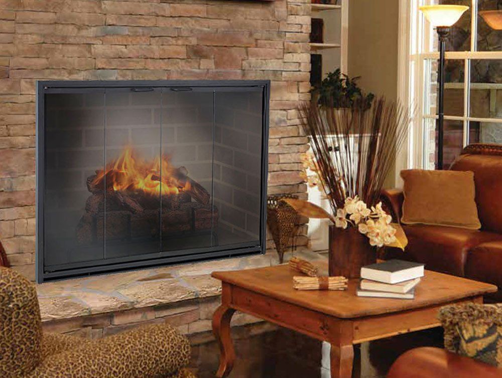 Fireplace with fire behind glass doors, brick and stone surround, wood table, and sofa.