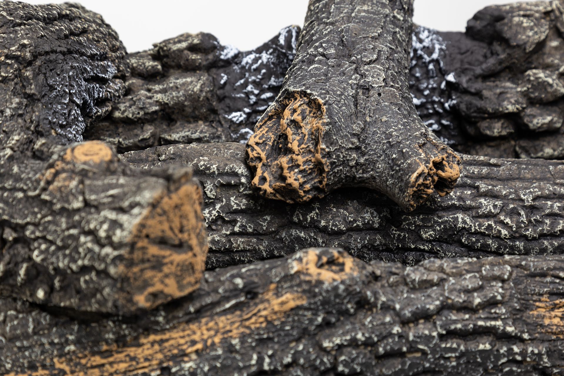 Close-up of a decorative fireplace log set. Gray, textured logs with brown details and a black background.