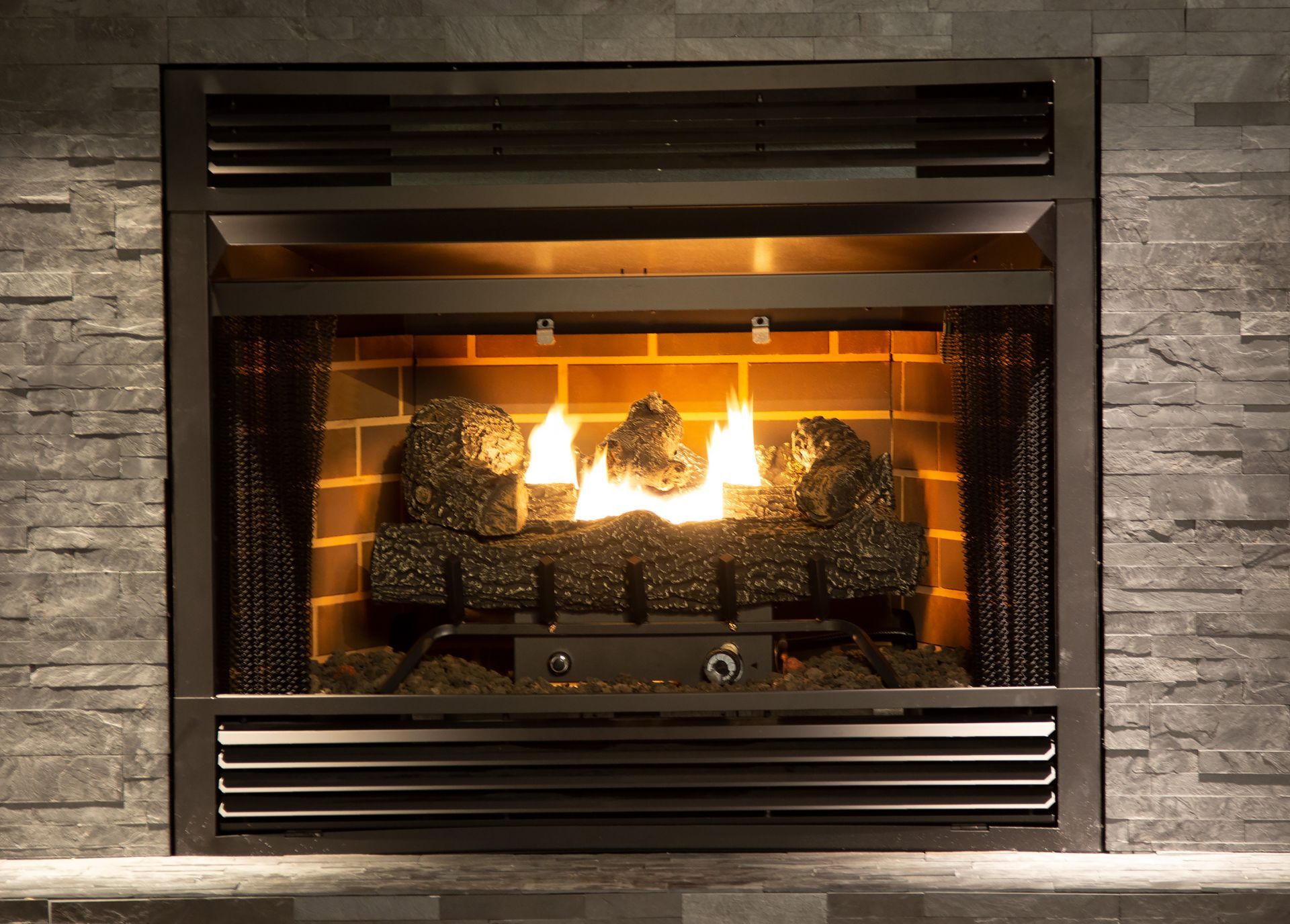 Gas fireplace with burning faux logs, brick background, grey stone surround.
