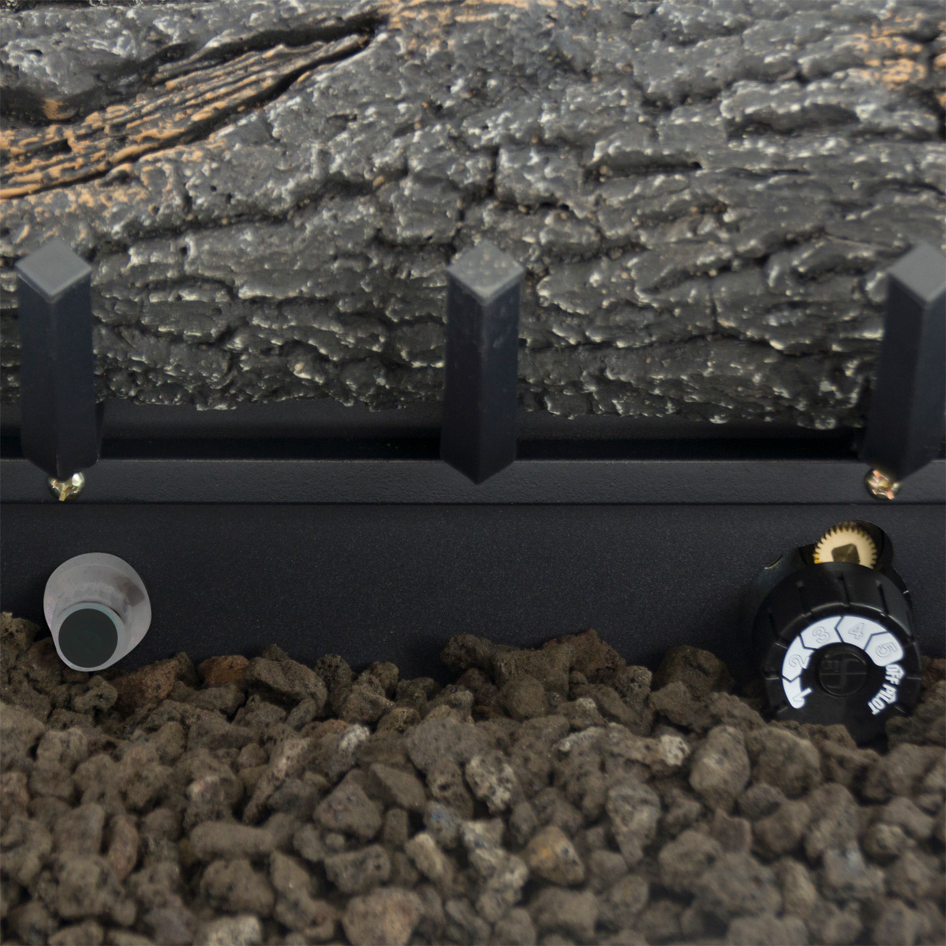 Close-up of gas fireplace log set with controls, black base, and lava rocks.