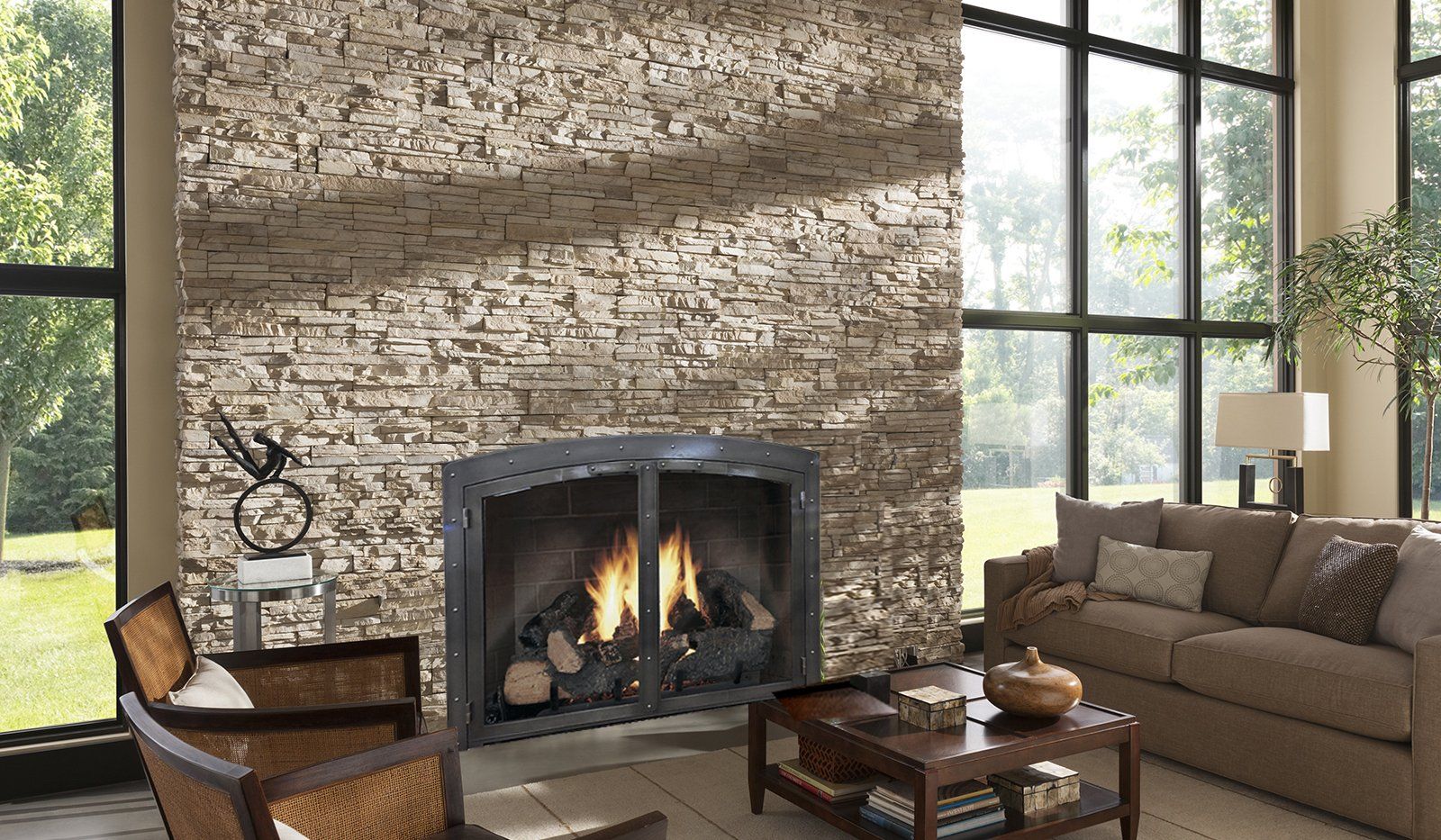 Living room with a stone fireplace, lit fire, sofa, chair, coffee table, and large windows.
