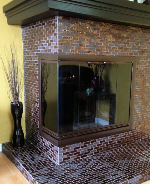 Fireplace with dark brown tile and glass doors, decorated with tall vase and branches.