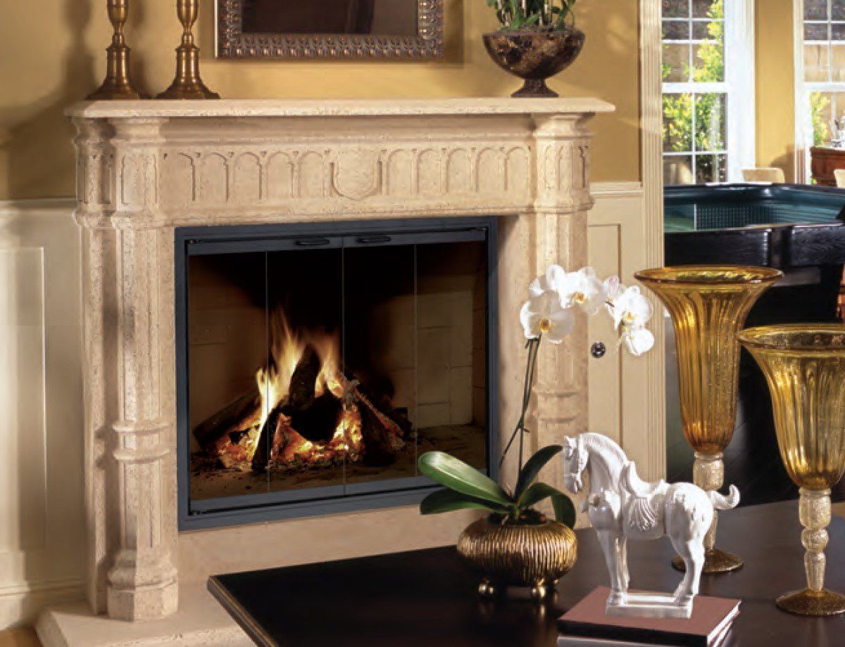 Fireplace with burning logs, stone mantel, glass doors, and decorative items on a dark table.