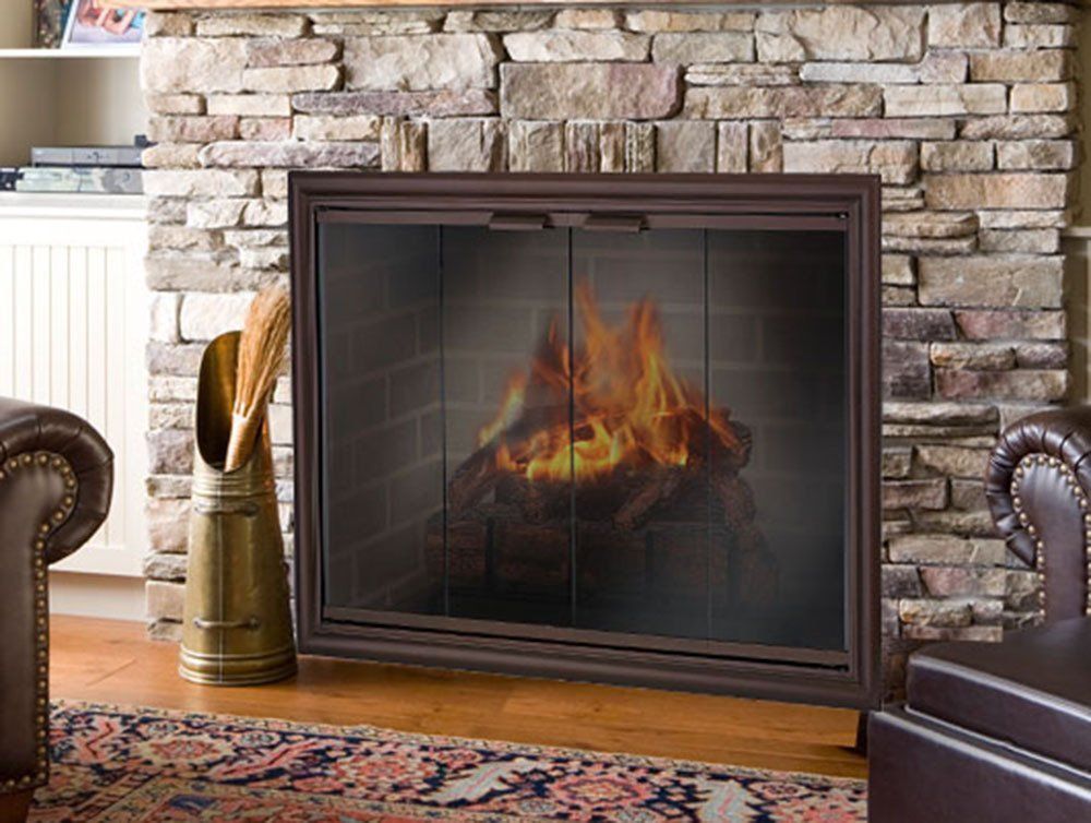 Fireplace with a burning fire behind glass doors, set in a stone wall.