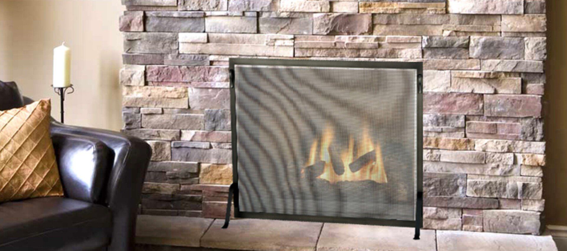 Fireplace with lit fire behind a mesh screen, in front of a stone wall. A couch is in the left corner.