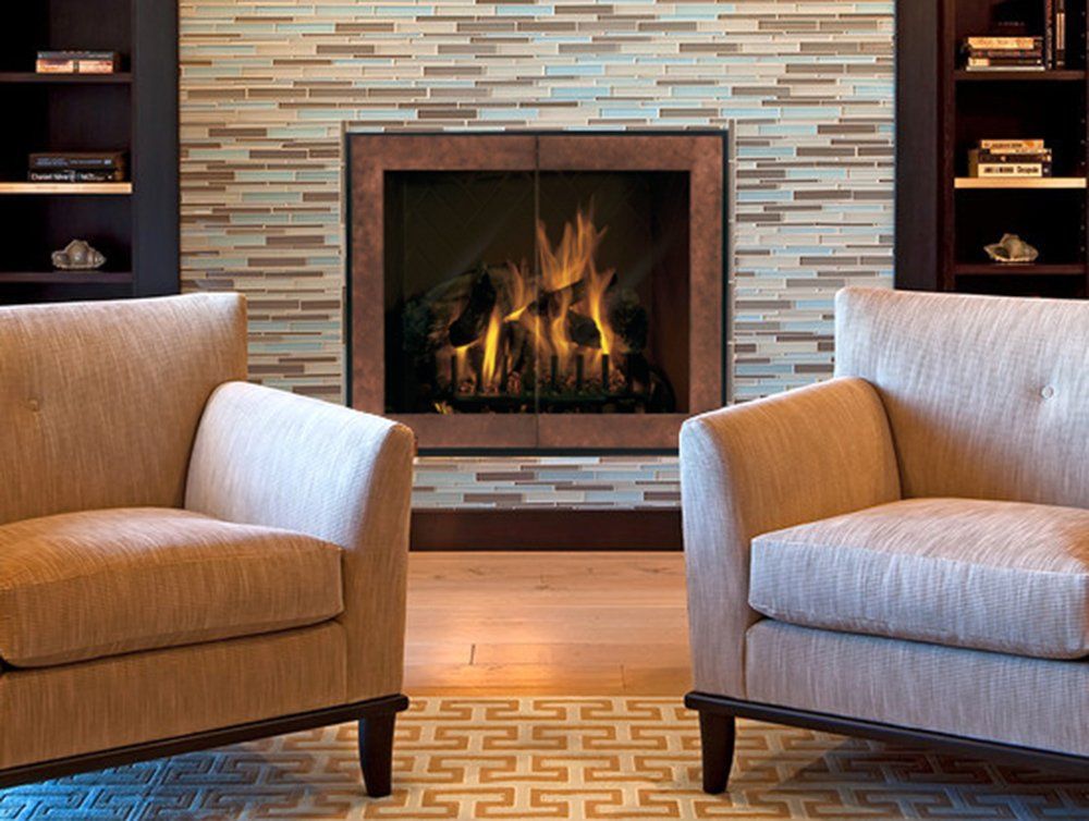 Two beige armchairs facing a fireplace with flames, built-in bookshelves, and a patterned rug.