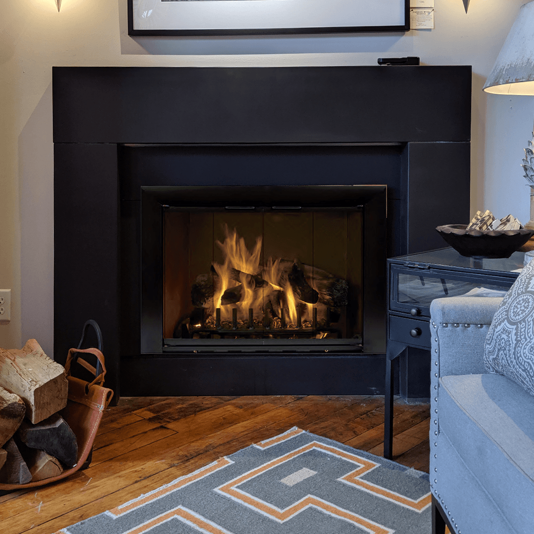 Fireplace with burning logs, black surround, wooden floor, and a gray patterned rug.
