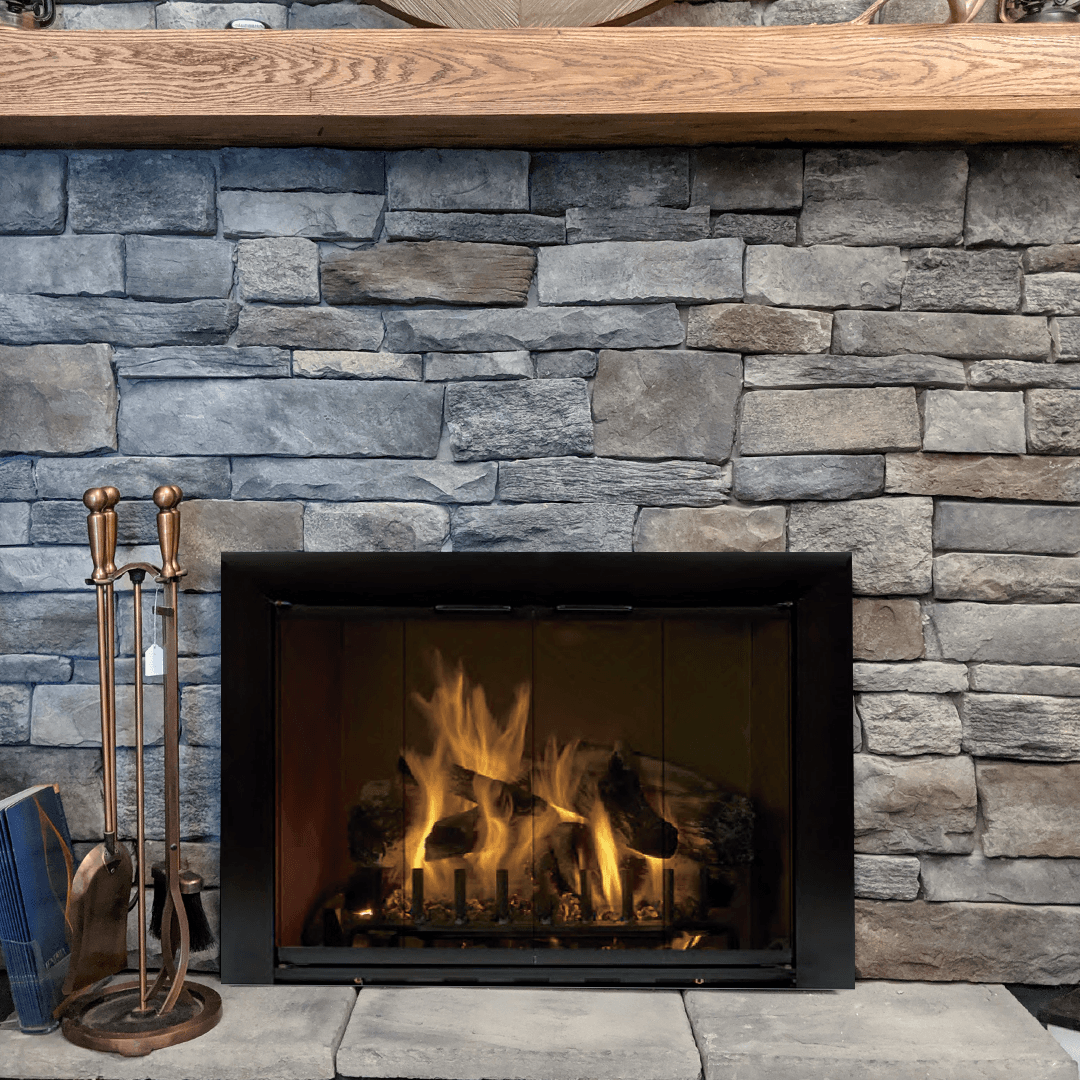 Fireplace with stone surround, lit fire, and copper tools. Wooden mantel above.