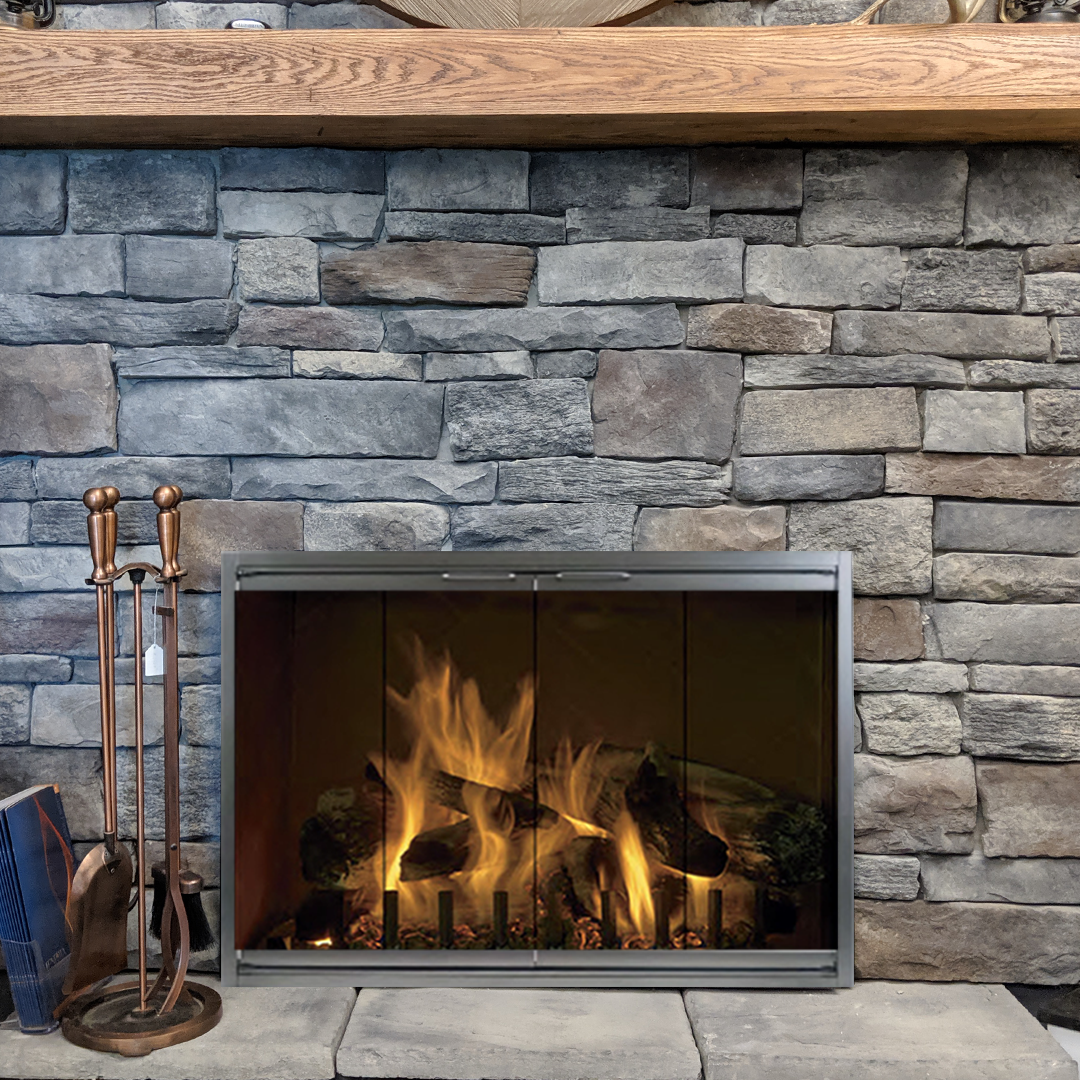 Fireplace with roaring flames inside, stone facade, and wooden mantle. Copper fire tools stand to the left.