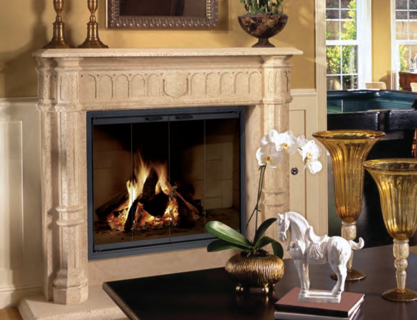 Fireplace with burning logs, ornate beige mantel, glass doors.  Orchids, horse statue, and vases on the table.