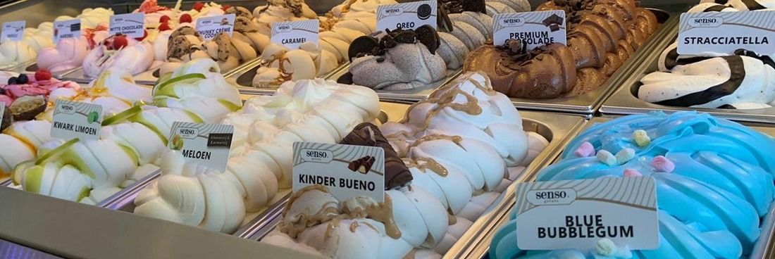 Een vitrine gevuld met diverse smaken kleurrijk ijs, waaronder blauwe kauwgomsmaak, voorzien van kleine prijskaartjes.