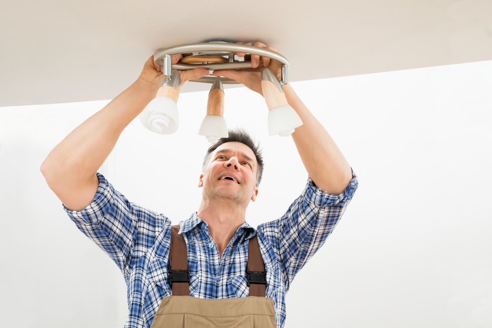 A Man is Installing a Light Fixture on the Ceiling — Mick Sawtell Electrical Pty Ltd in Kyogle, NSW