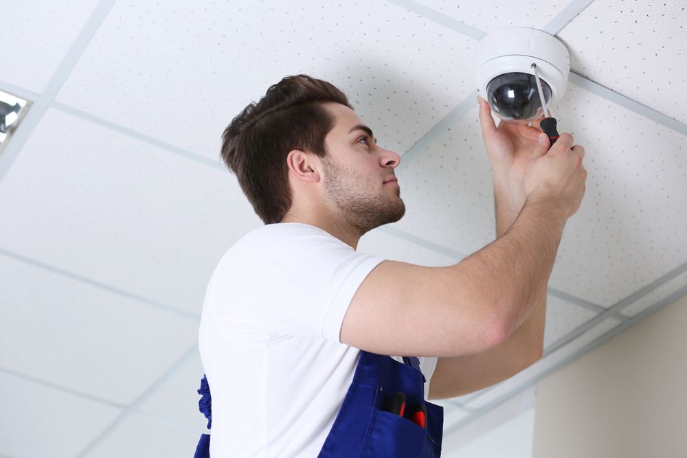 A Man is Installing a Security Camera on the Ceiling — Mick Sawtell Electrical Pty Ltd in Palm Beach, QLD
