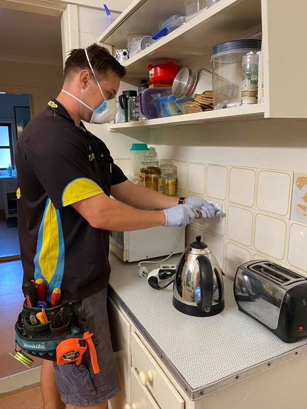 A Man Wearing a Mask and Gloves is Working in a Kitchen — Mick Sawtell Electrical Pty Ltd in Palm Beach, QLD
