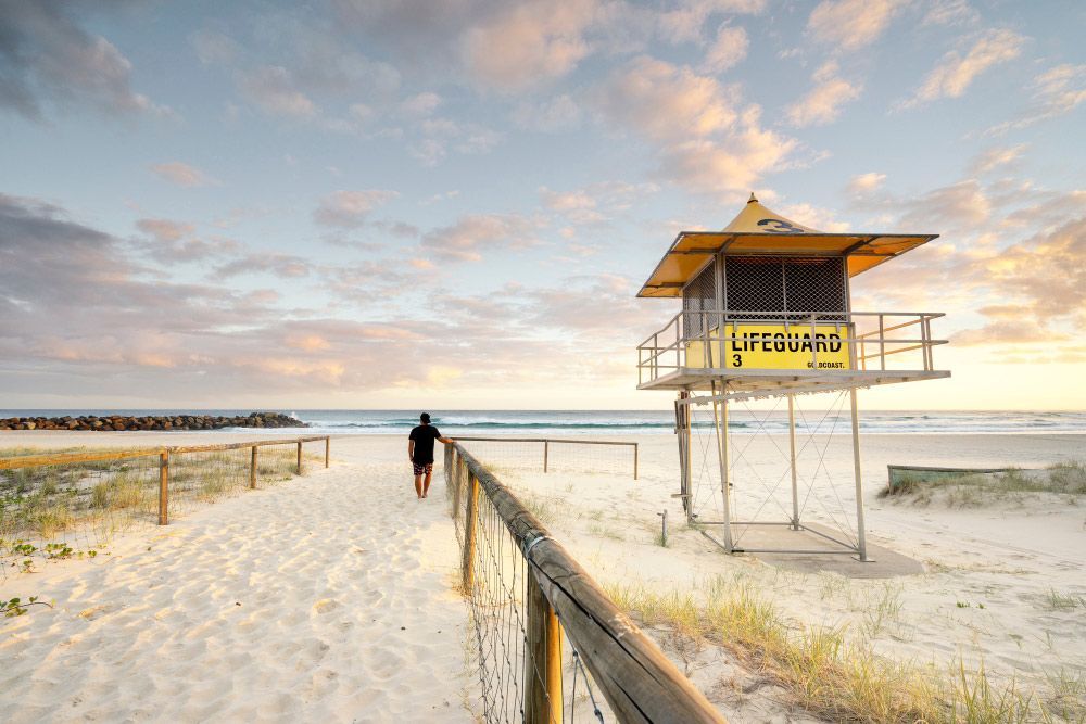 A Man is Walking Towards a Lifeguard Tower on a Beach — Mick Sawtell Electrical Pty Ltd in Coolangatta, QLD