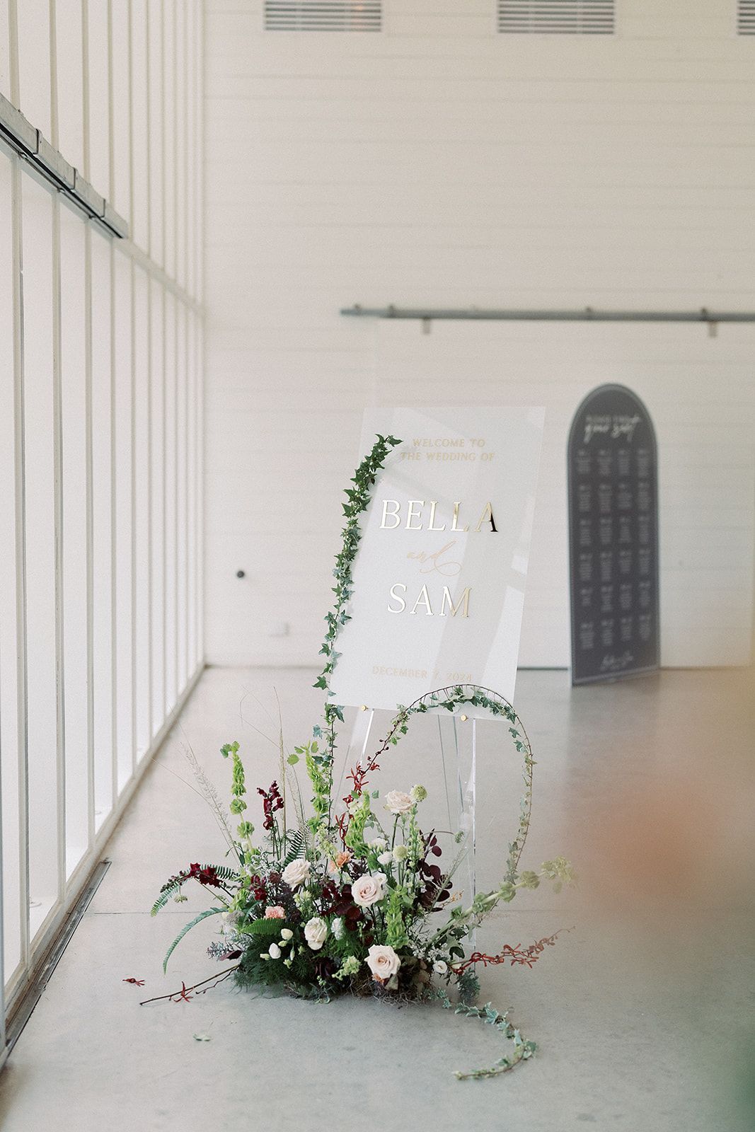 Floral arrangement in a white gallery-like hallway beside a leaning sign and arched doorway.