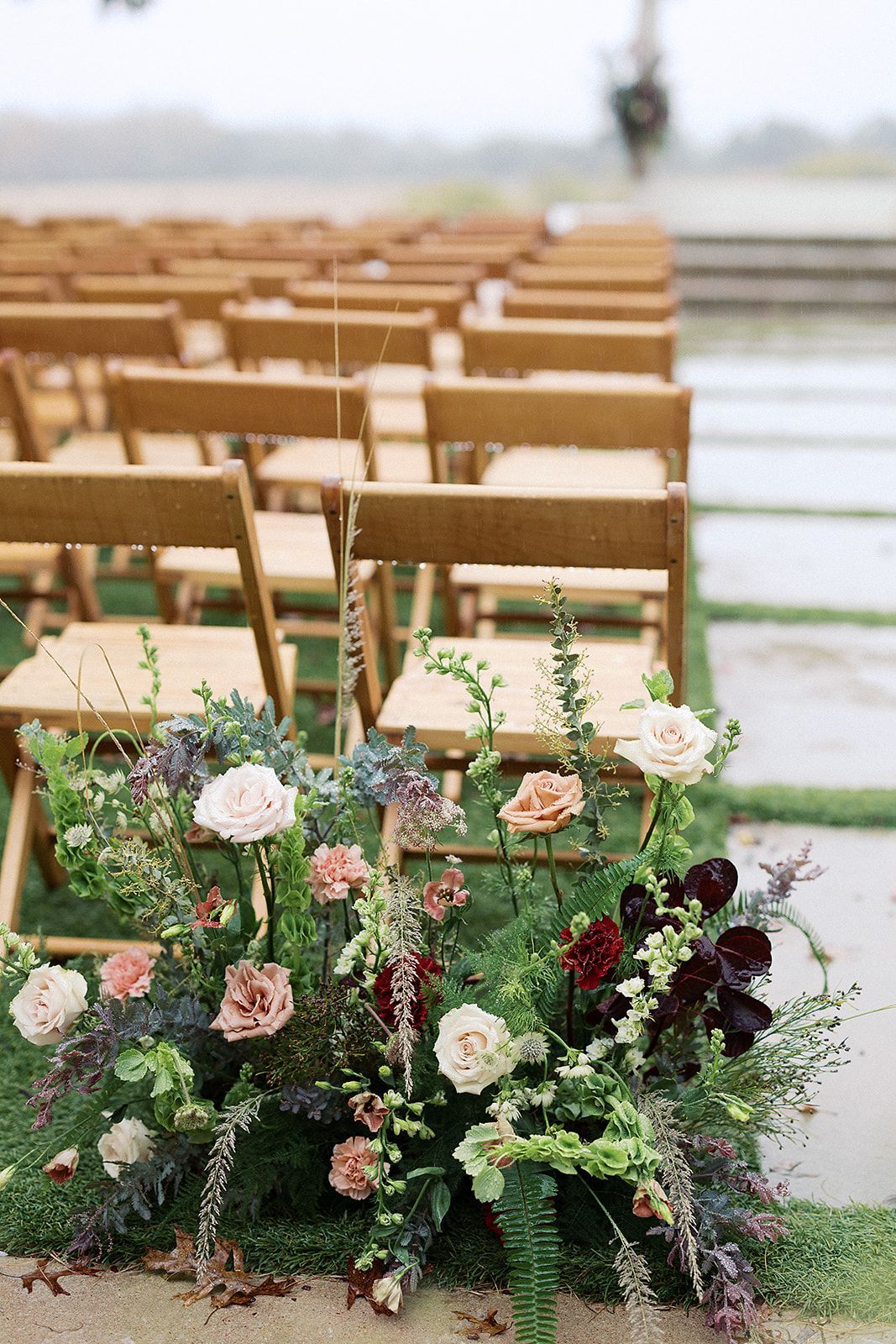 Floral arrangement at the front of outdoor wooden chairs on a grassy wedding aisle