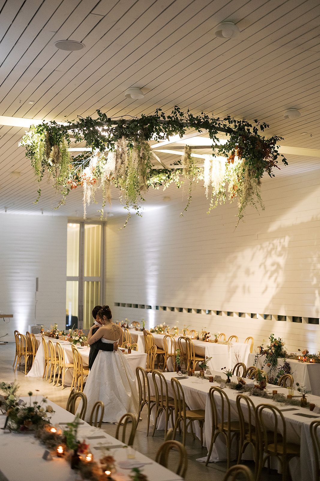 Elegant wedding reception hall with hanging greenery, candlelit tables, and a bride in a white gown