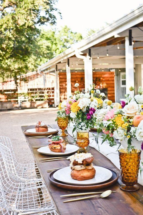 Elegant outdoor table setting with floral centerpieces, amber glassware, and plated desserts on a patio