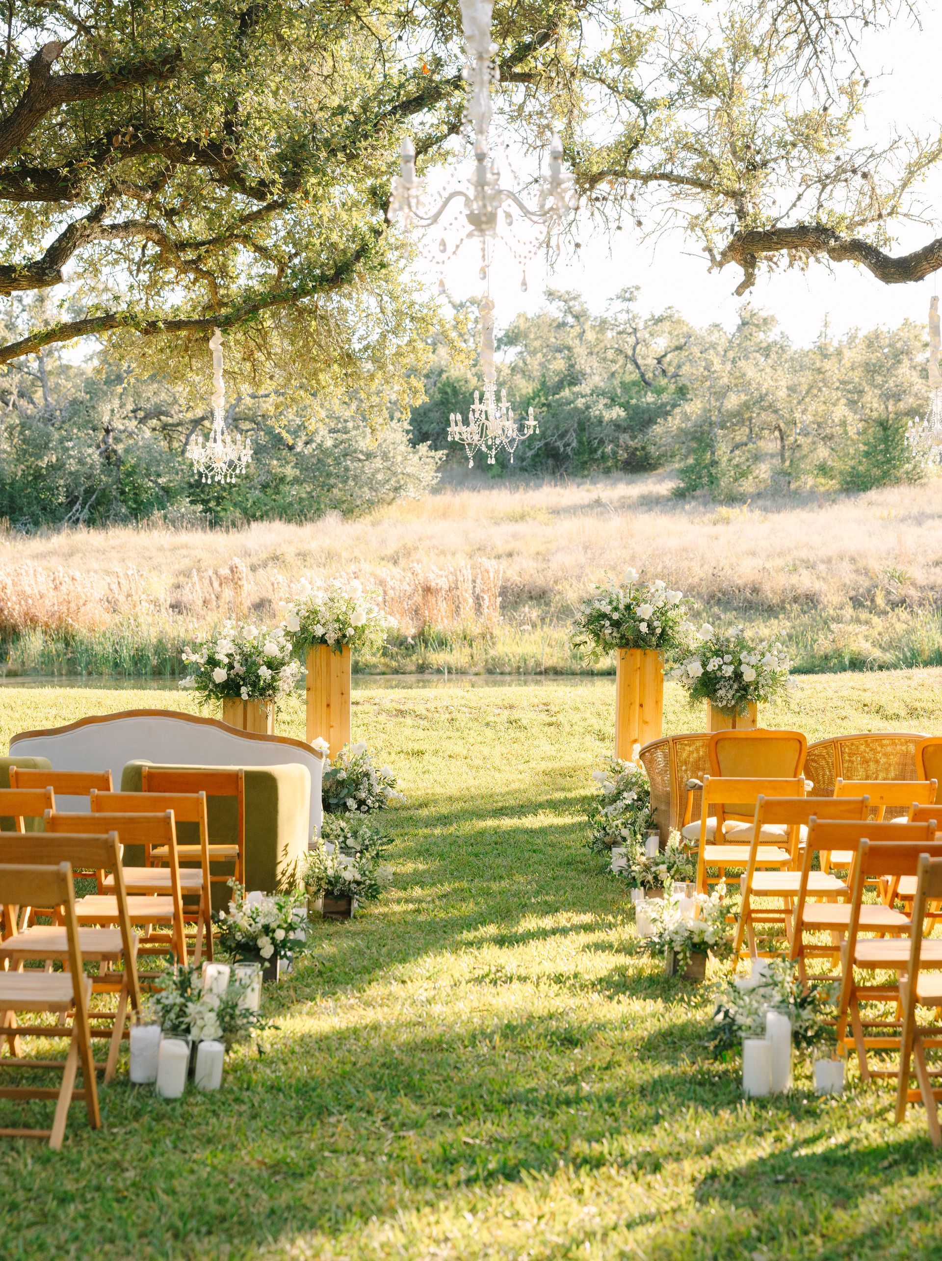 Outdoor wedding ceremony setup with wooden chairs on a grassy aisle under trees