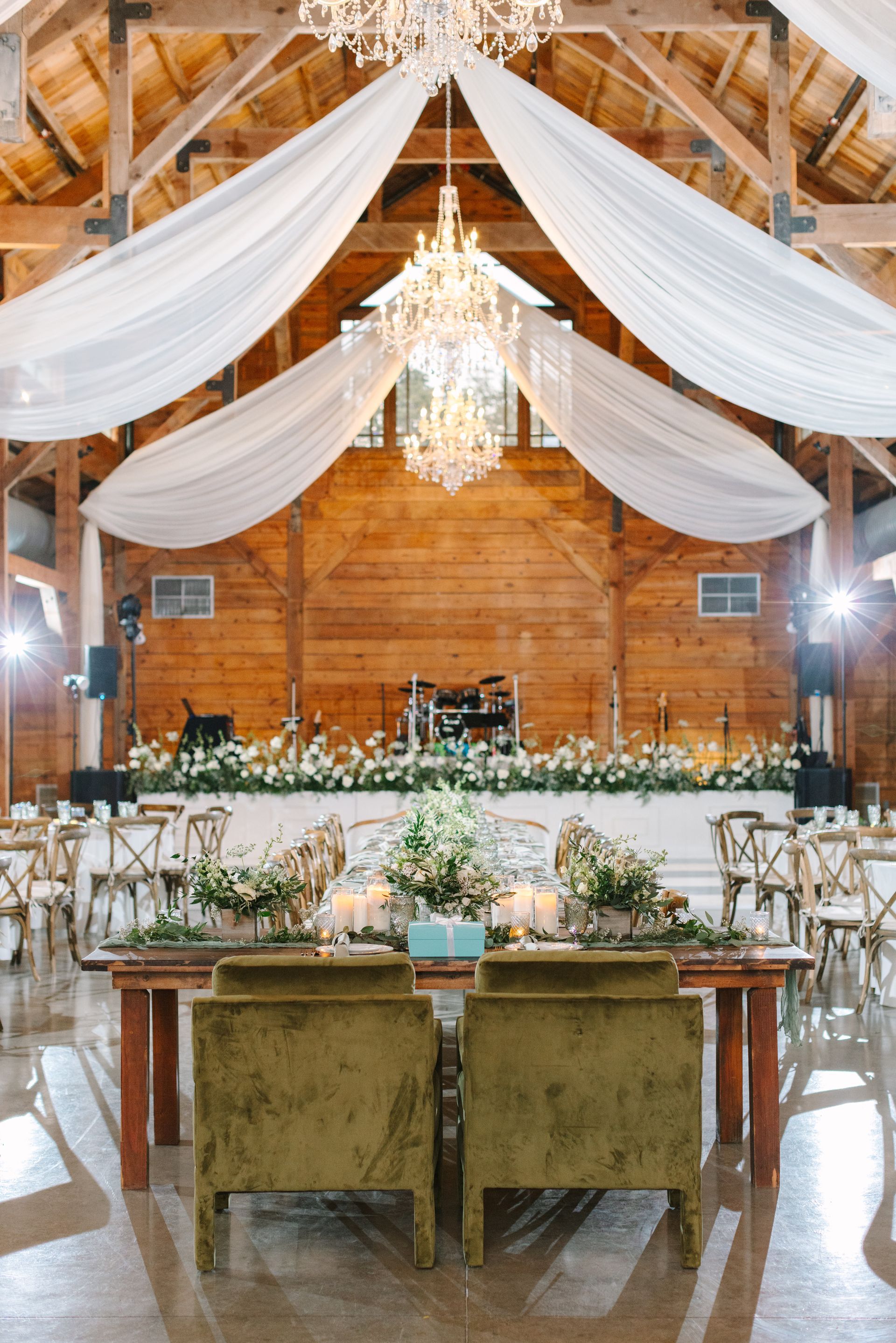 Rustic barn wedding reception setup with draped white fabric, chandelier, and decorated head table