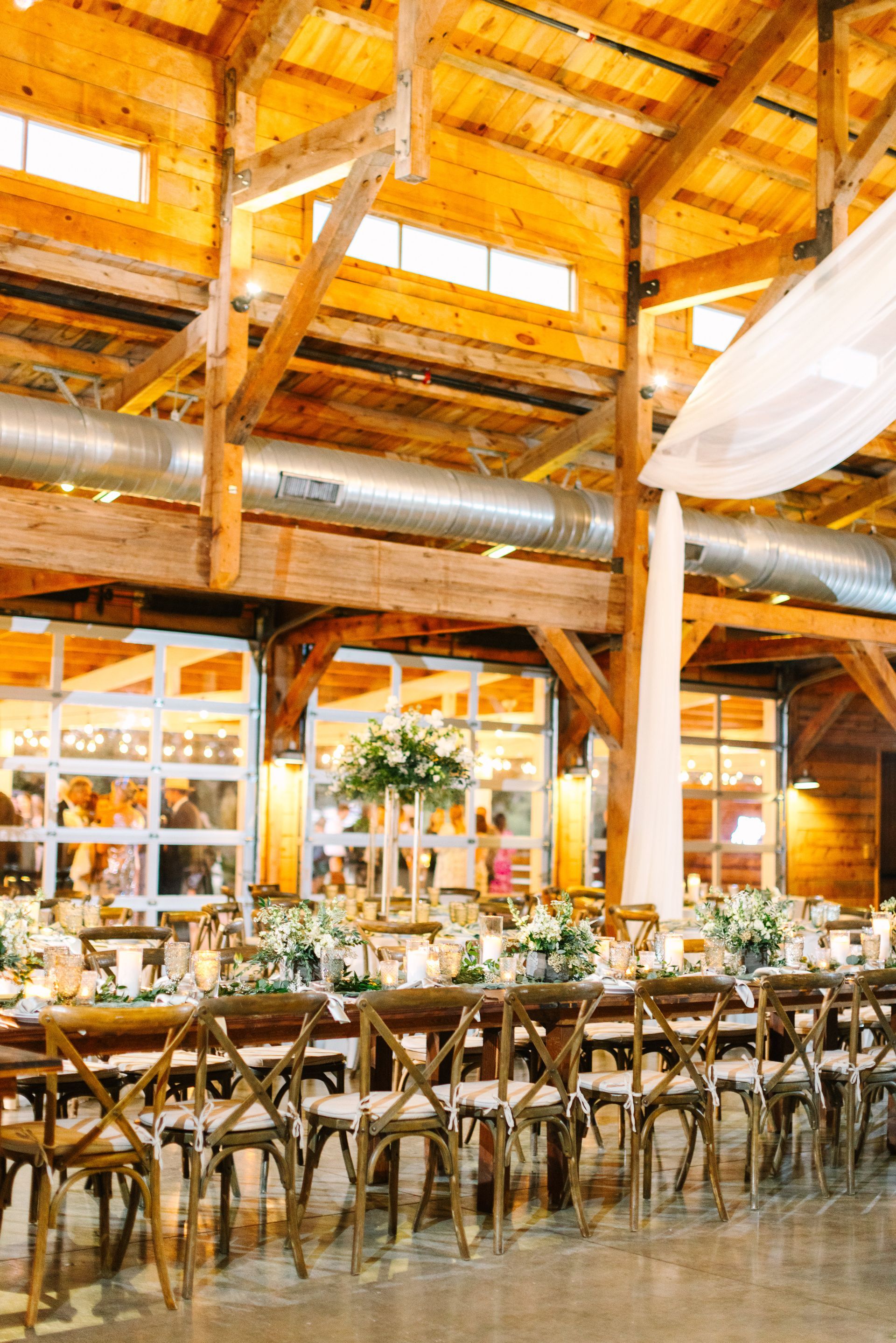 Rustic event hall with wooden beams, long tables, and hanging lights in warm amber tones