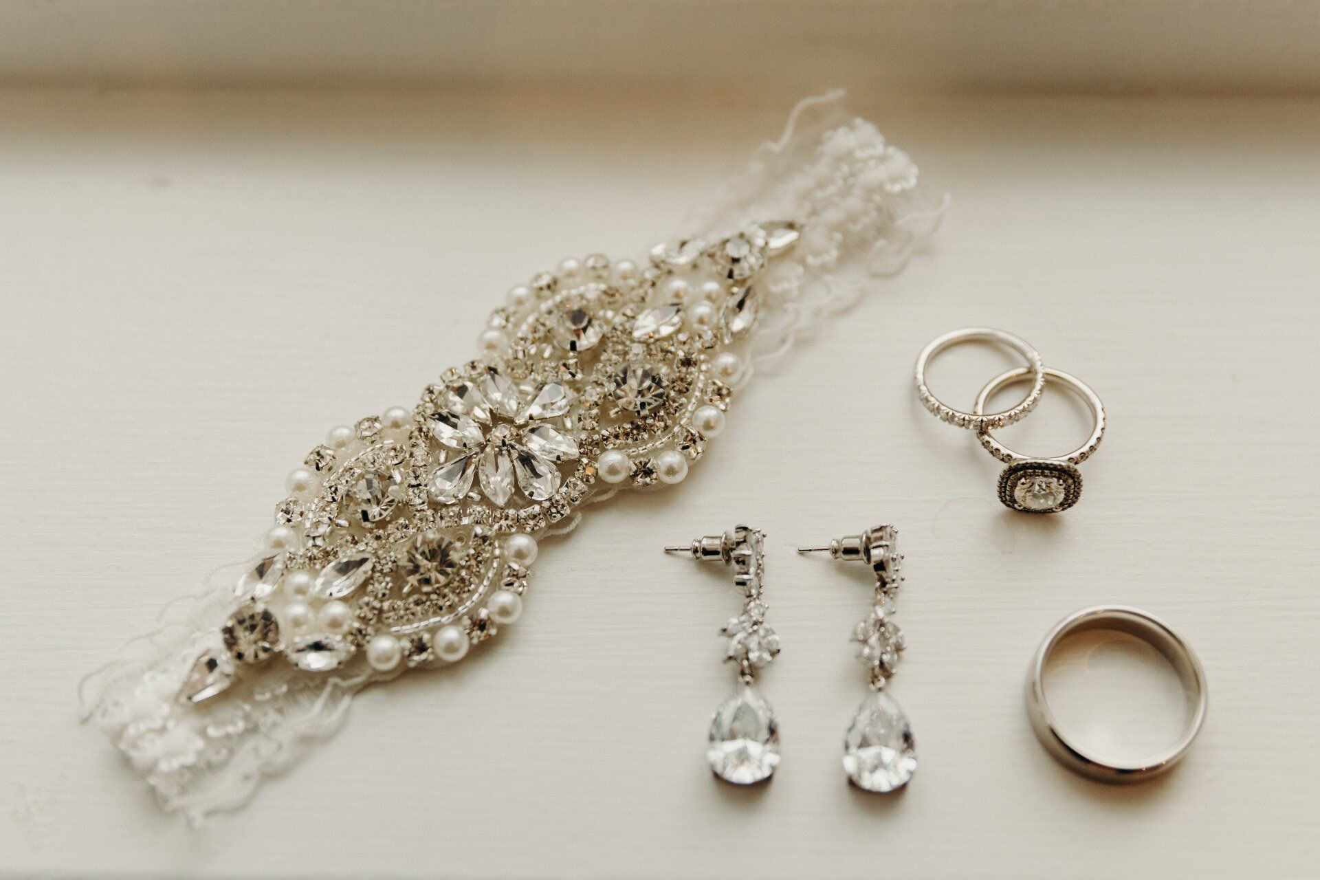 Bridal jewelry set with jeweled headpiece, earrings, and rings on a light background