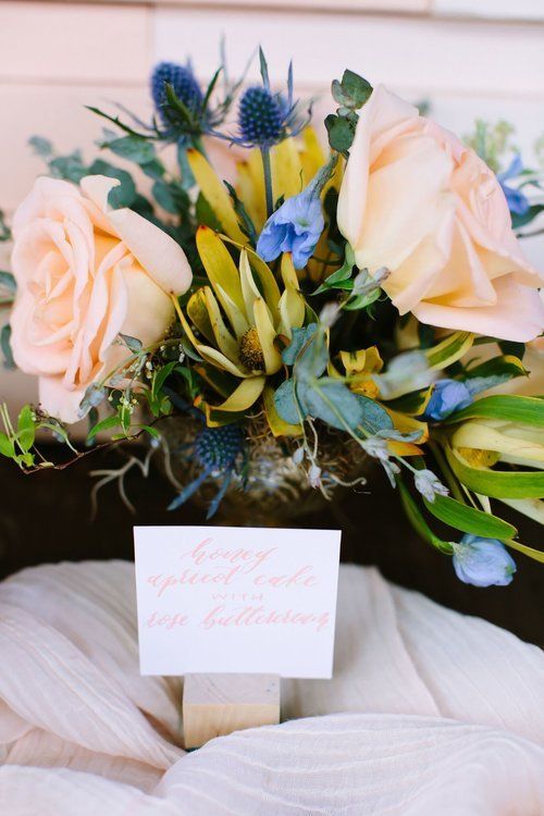 Bouquet of cream roses and blue flowers in a vase with a small card on a white cloth