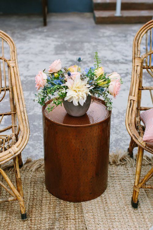 Floral arrangement in a vase on a wooden table between wicker chairs outdoors