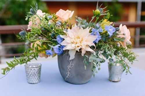 Pastel floral arrangement in a gray vase with two small votive holders on a table
