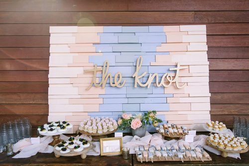 Dessert table with cupcakes and cookies in front of a white and blue backdrop reading “the knot”