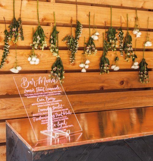 Wooden menu display with hanging greenery and a clear acrylic sign in a rustic setting