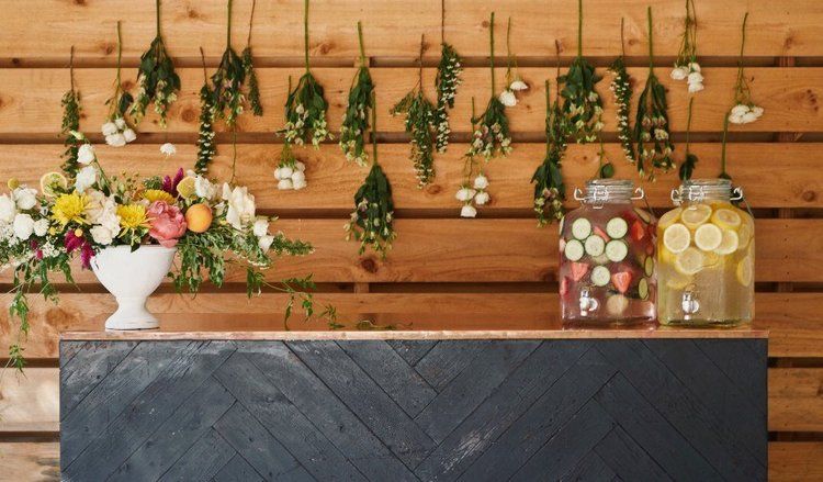 Rustic dessert and floral display on a wooden backdrop with hanging greenery and glass jars of colorful treats