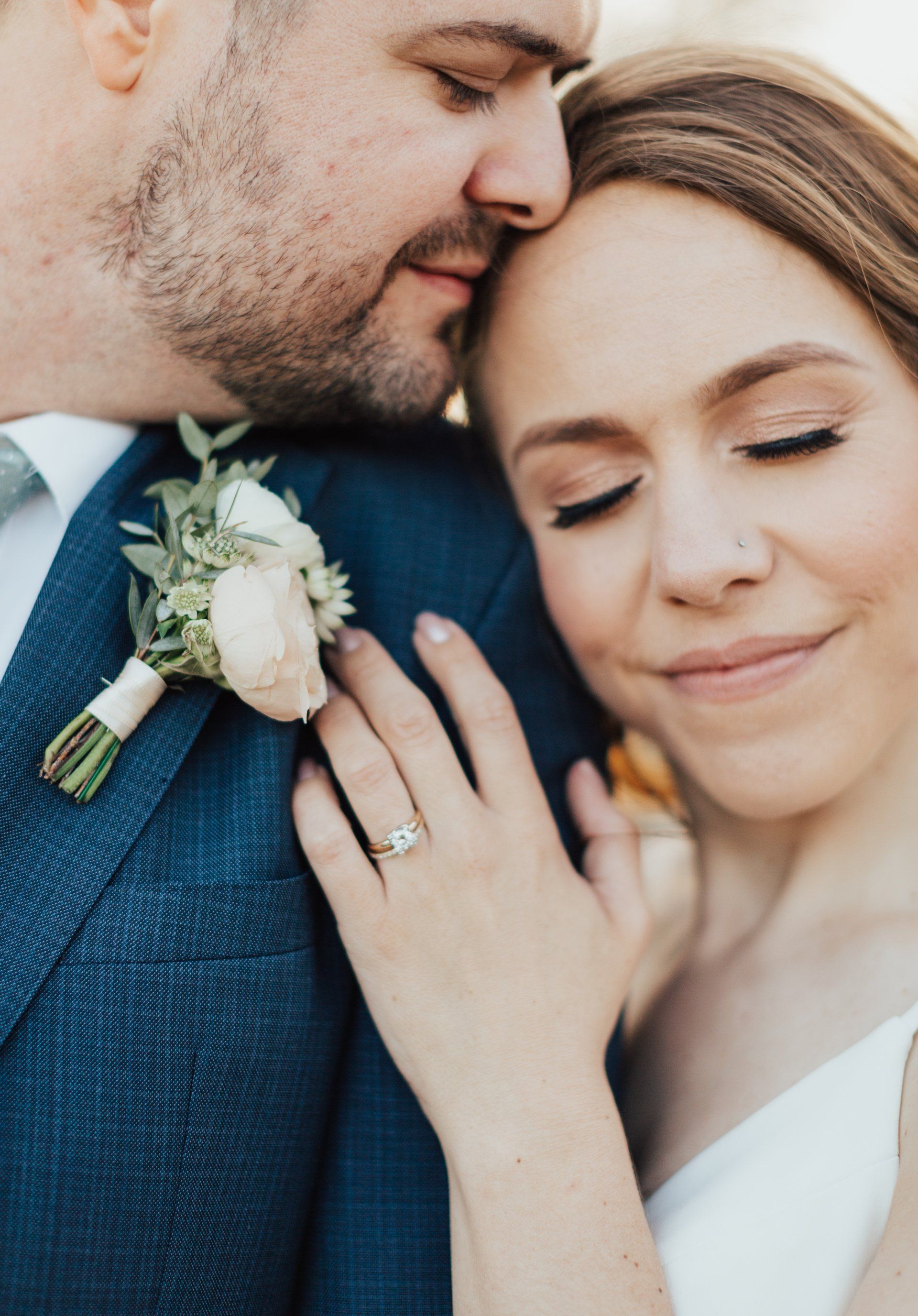 Close-up of a couple embracing, with the bride smiling and her engagement ring visible