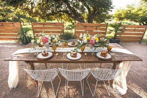 Outdoor dining table with floral centerpiece, plates, and woven chairs in a garden setting