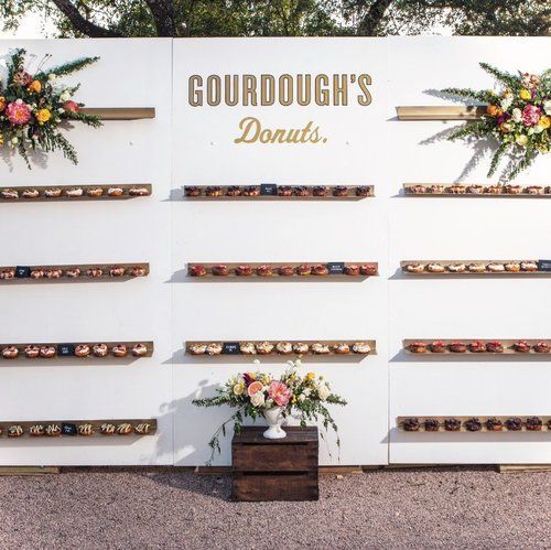 Gourdough’s Donuts wall display with rows of donuts and floral arrangements on a white backdrop