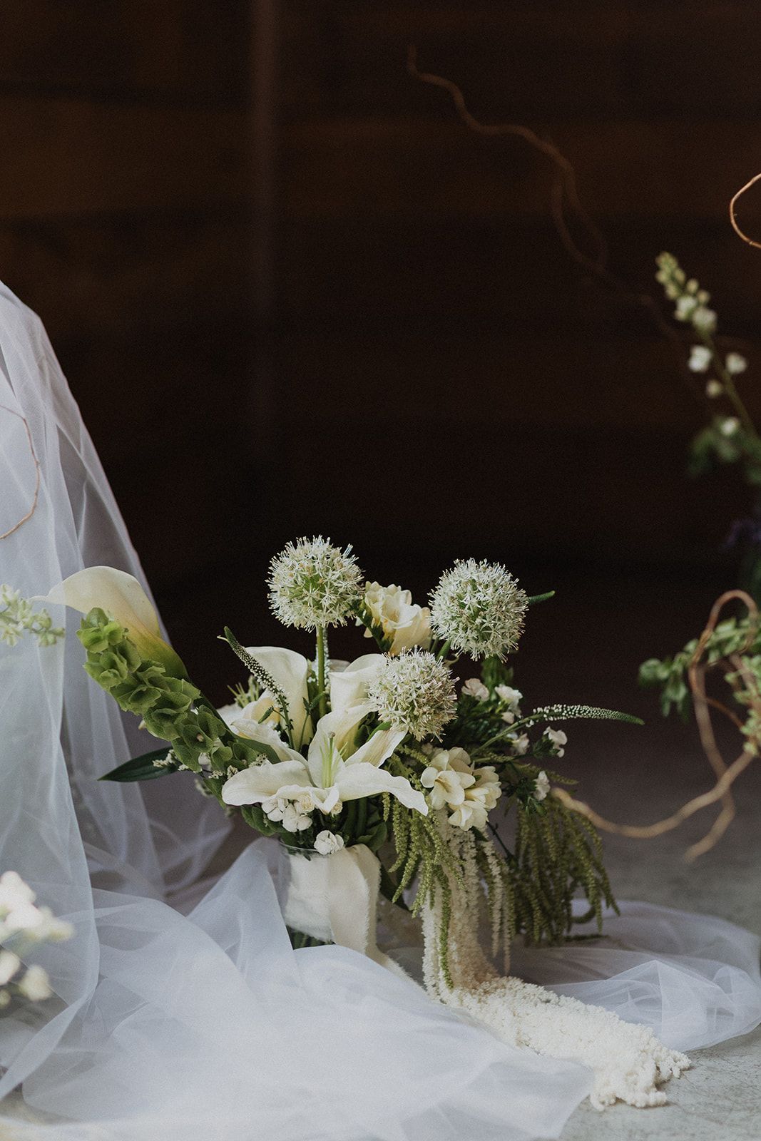 White bridal bouquet with lilies and round blooms on draped fabric in a dark background