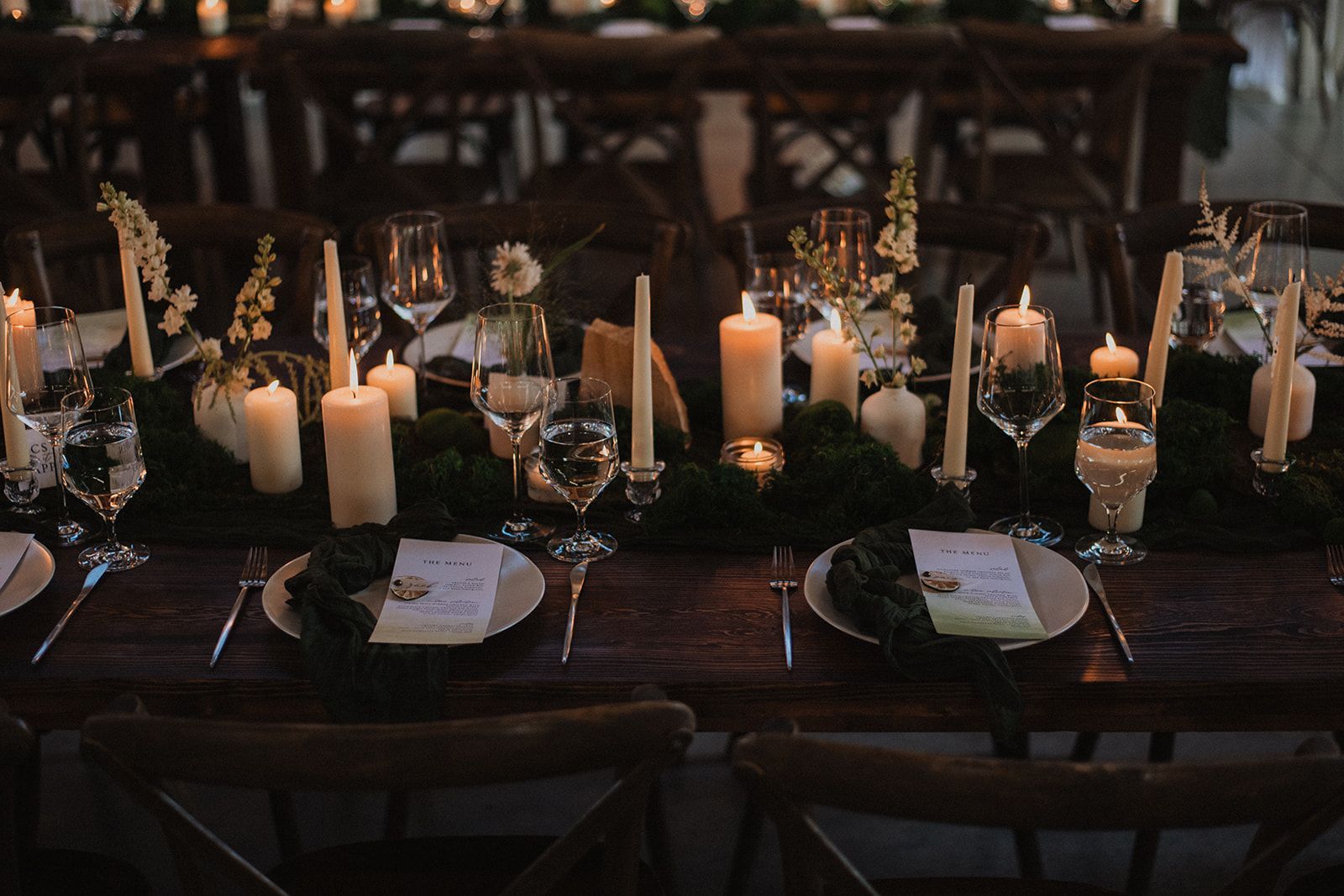 Dimly lit banquet table with candles, glassware, and dark place settings