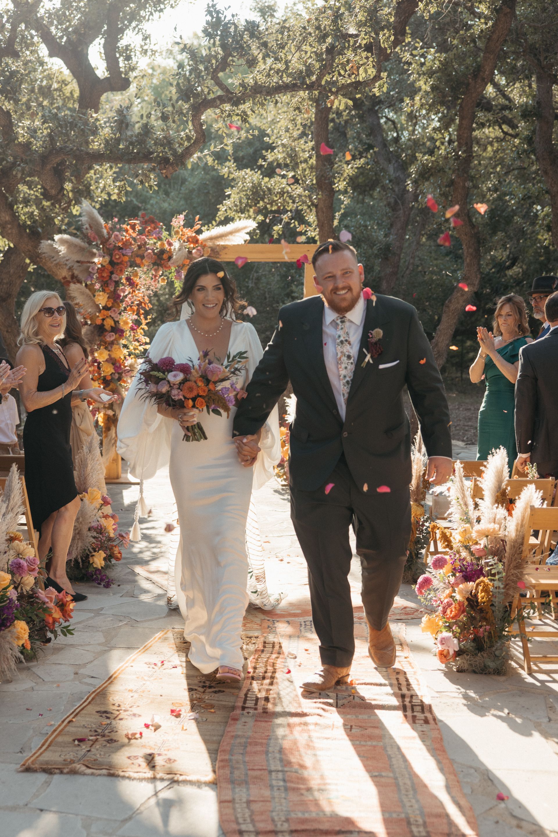 Bride and groom walking down a flower-lined outdoor aisle at a wedding ceremony