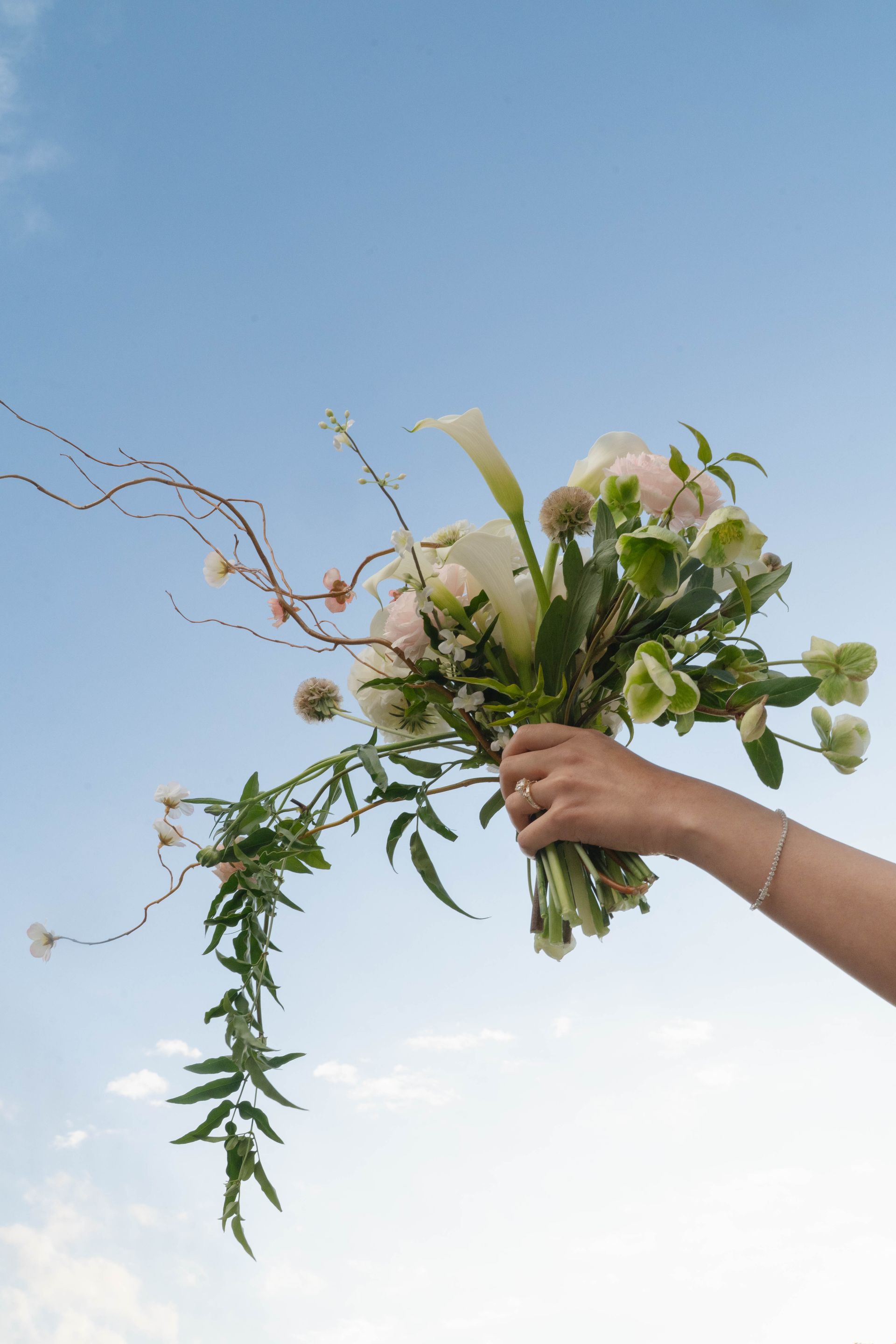 Hand holding a bouquet of white flowers and greenery against a clear blue sky