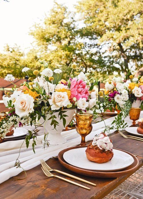 Elegant outdoor table setting with floral centerpiece, gold accents, and pastries on white plates
