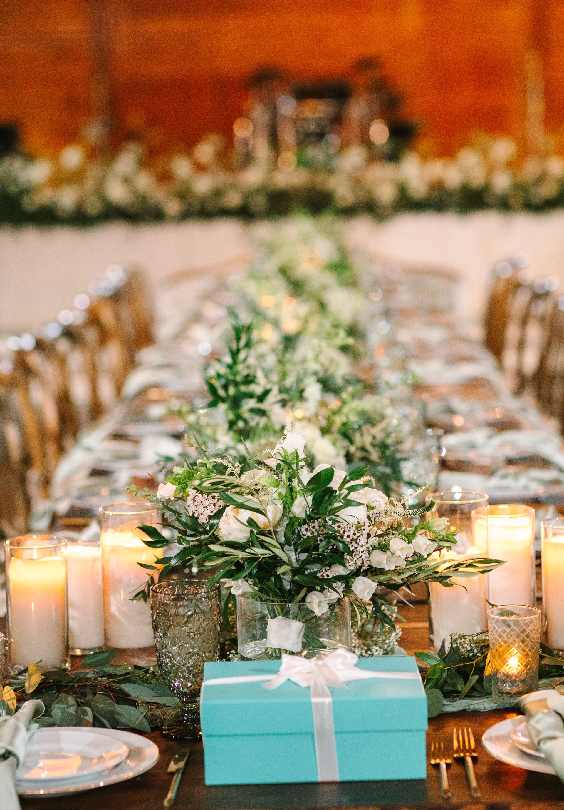 Elegant banquet table with white floral runners, candles, and a turquoise gift box centerpiece
