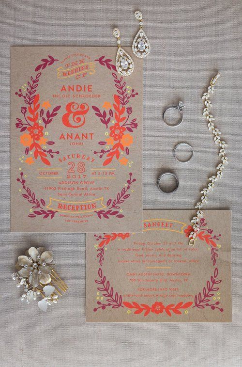 Pink floral wedding invitation suite with rings, earrings, bracelet, and gold-accented envelope on gray fabric
