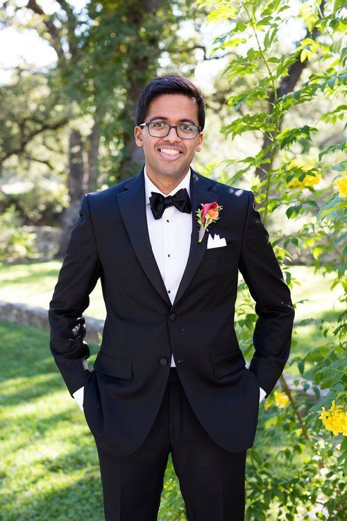 Smiling man in a black tuxedo standing outdoors in a sunlit garden