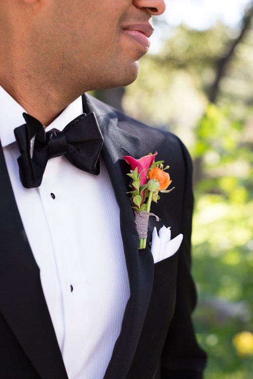 Close-up of a groom in a black tuxedo with a red boutonniere and white pocket square outdoors