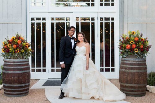Newlywed couple posing outside white doors with autumn flower arrangements