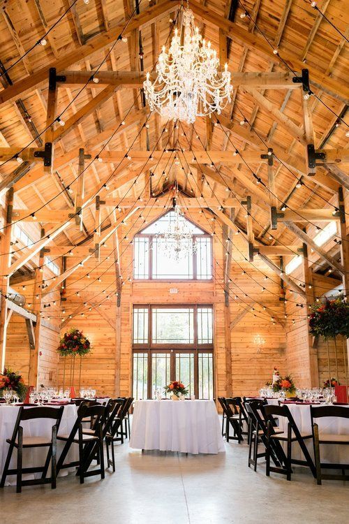 Barn interior with exposed wood beams, a chandelier, and a decorated reception table setup