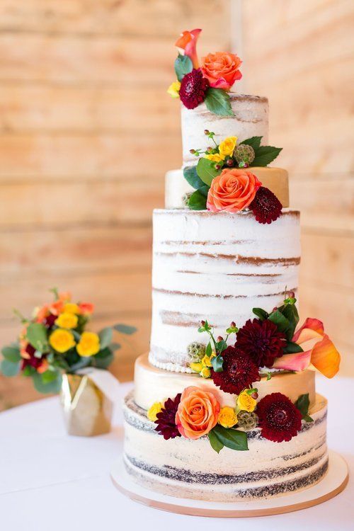 Three-tier white wedding cake with orange, red, and yellow flowers on a wooden cake stand