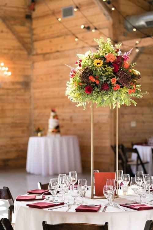 Floral centerpiece on a round dining table in a rustic banquet hall, with white tablecloths and glassware